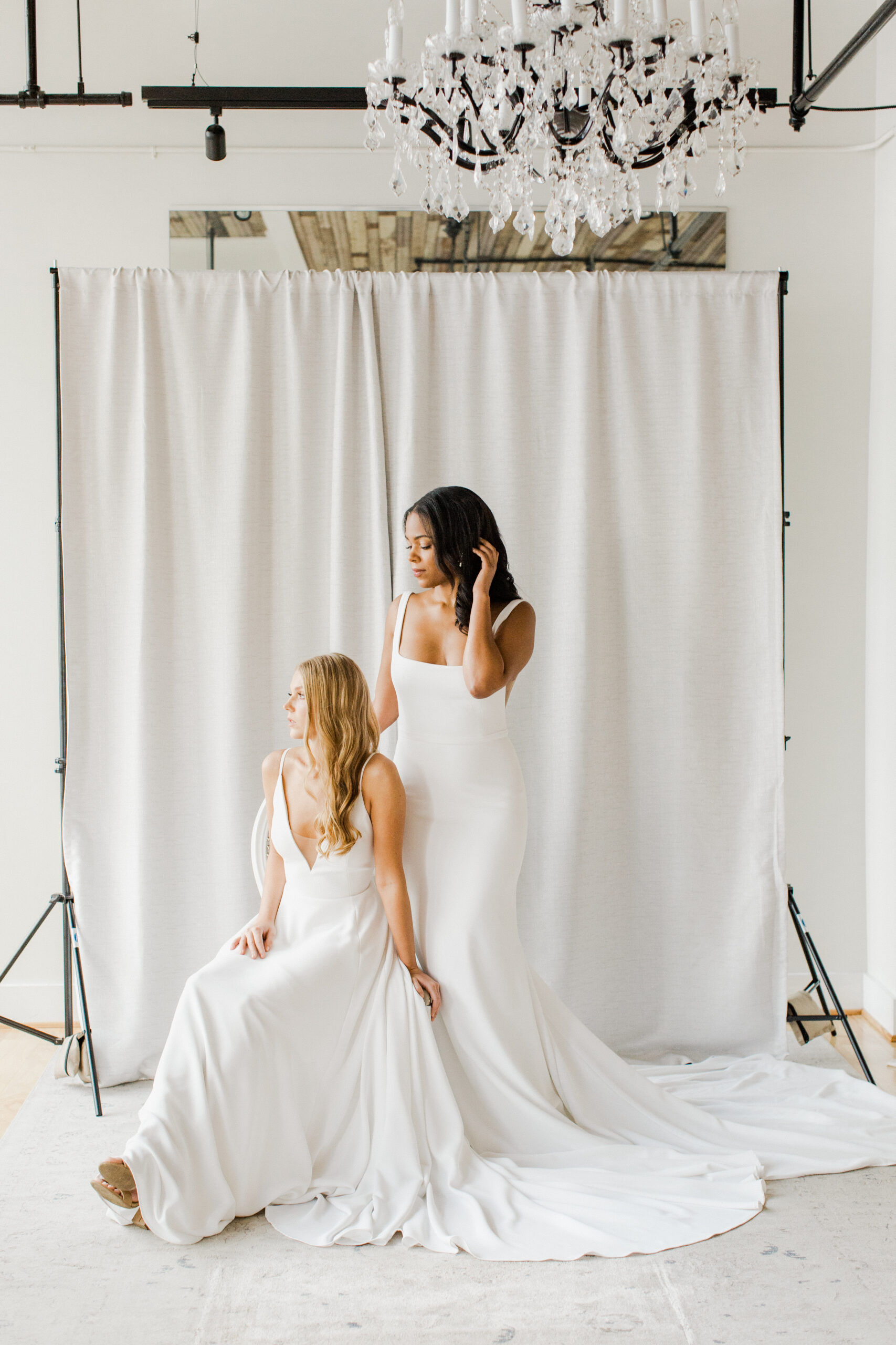 Two bridal models standing in front of photoshoot backdrop in simple wedding dresses.